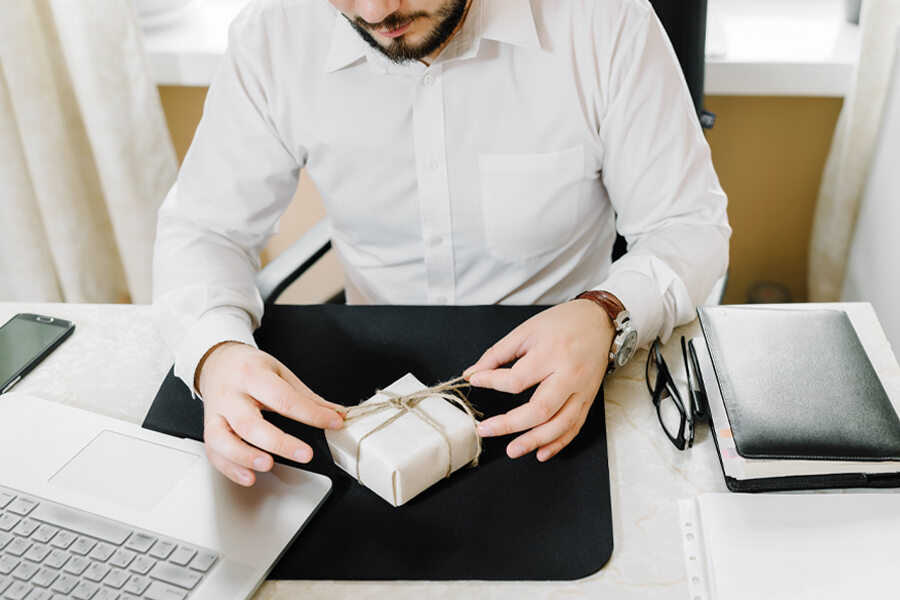 A man in a white shirt sits at a desk, holding a gift wrapped in a box