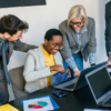 A diverse group of business professionals collaborating on a laptop, surrounded by employee chocolate gifts on the table