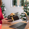 A woman holds a gift box in one hand and a laptop in the other, symbolizing corporate gifting solution