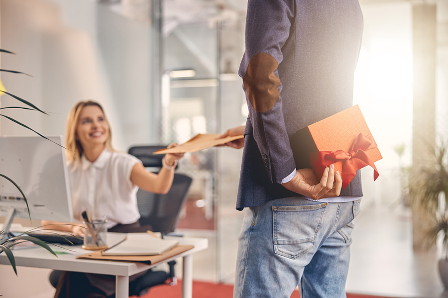 A man presents a gift to a woman in an office setting, showcasing a moment of appreciation and celebration